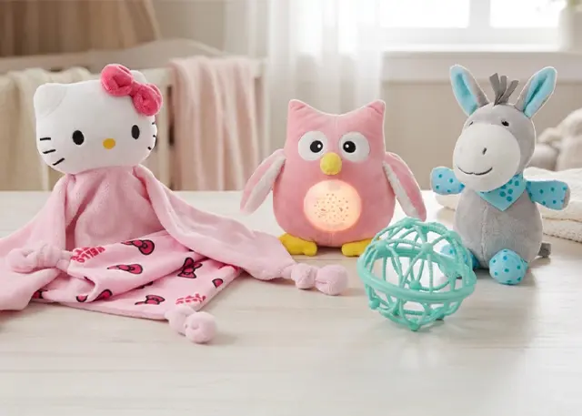 Eine gemütliche Anordnung von Plüschtieren: eine Hello-Kitty-Decke, eine rosa Eule mit Licht, ein grauer Esel und ein petrolfarbener Ball, alles auf einem Holztisch. Eine gemütliche Anordnung von Plüschtieren: eine Hello-Kitty-Decke, eine rosa Eule mit Licht, ein grauer Esel und ein petrolfarbener Ball, alles auf einem Holztisch.