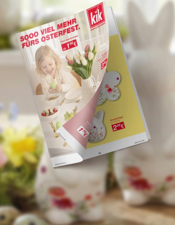 Dekorative Frühlingsszene mit drei weißen Hasenfiguren, bunten Blumen und einem Werbeflyer für Osterartikel.