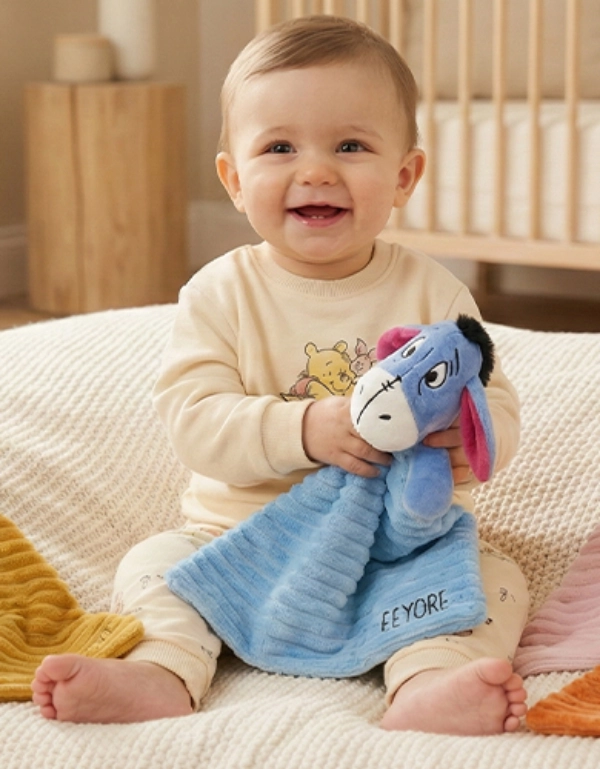 Ein Kind sitzt auf einer kuscheligen Decke, umgeben von bunten Plüschtieren und Decken, die eine warme und verspielte Atmosphäre schaffen.