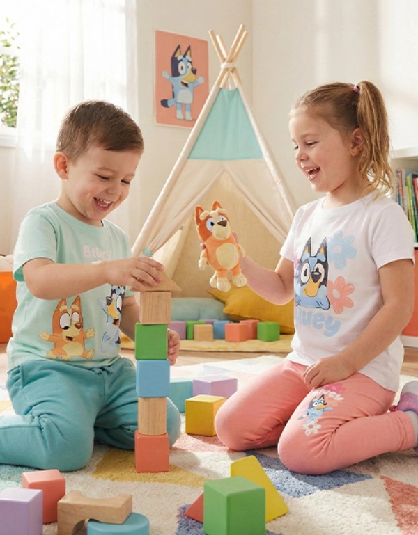 Zwei Kinder spielen gemeinsam auf einem bunten Teppich, stapeln Bauklötze und halten ein Spielzeug in einem hellen und fröhlichen Raum.