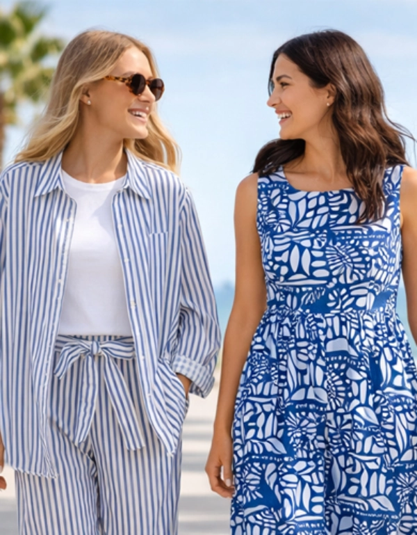 Zwei Frauen, die auf einem sonnigen, von Palmen gesäumten Strandweg spazieren gehen und sich unterhalten, im Hintergrund das Meer.