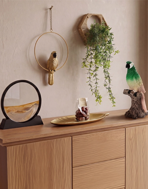 Dekorative Wohnaccessoires mit Papageienfiguren, Wanddeko und Hängepflanze auf einer Holzkommode im Dschungel-Look