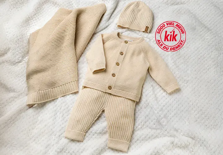 Ein weiches Babyoutfit in Beige mit Strickjacke, Hose und passender Mütze, präsentiert auf einer strukturierten Decke.